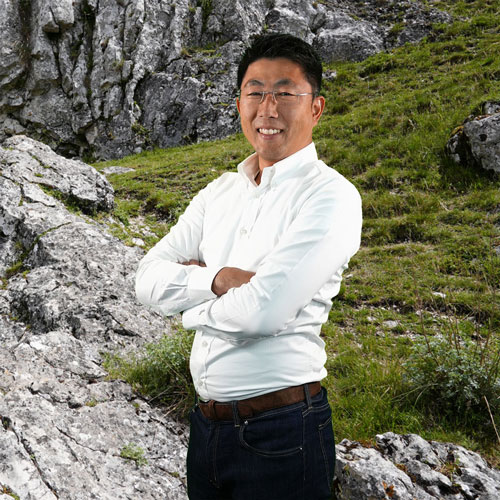 Close-up of Moto Dohi, outdoors, in a white shirt, smiling.