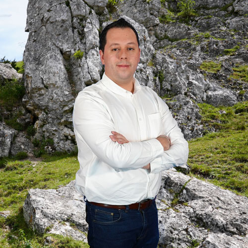 Close-up of Carlos Mayorga, outdoors, in a white shirt, smiling.