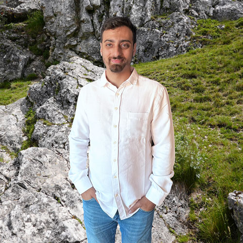 Close-up of Denizhan Soydaş, outdoors, in a white shirt, smiling.