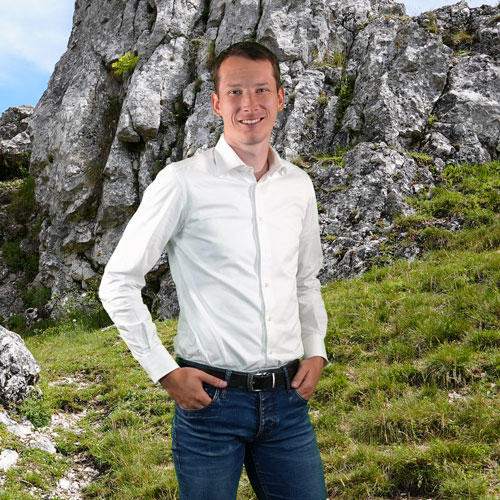 Close-up of Hans Leupold, outdoors, in a white shirt, smiling.