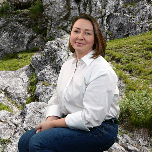 Close-up of Kristina Brinster, outdoors, in a white shirt, smiling.