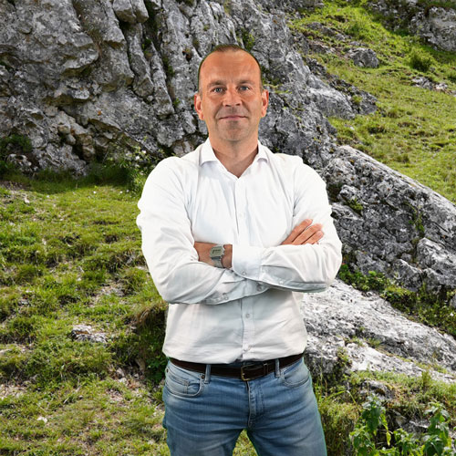 Close-up of Patrick König, outdoors, in a white shirt, smiling.