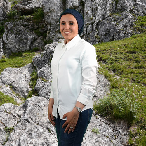 Close-up of Rania Hassanain, outdoors, in a white shirt, smiling.