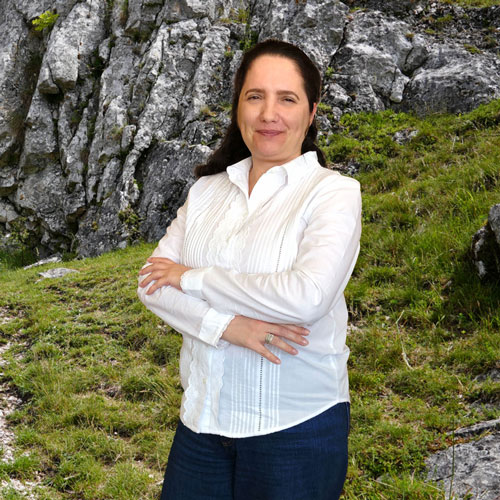 Close-up of Débora Pinto, outdoors, in a white shirt, smiling.