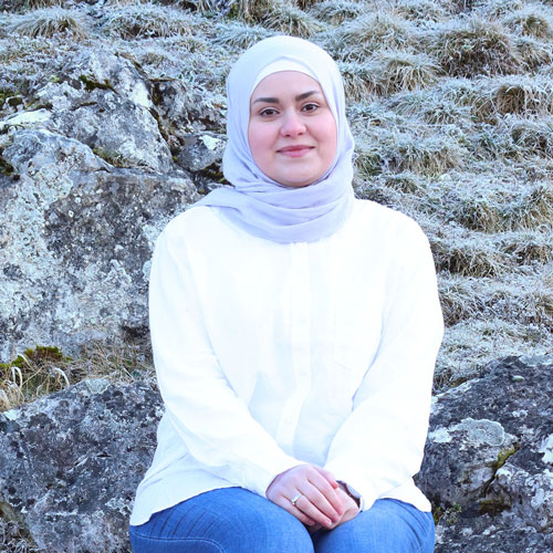 Close-up of Douaa Hussien, outdoors, in a white shirt, smiling.