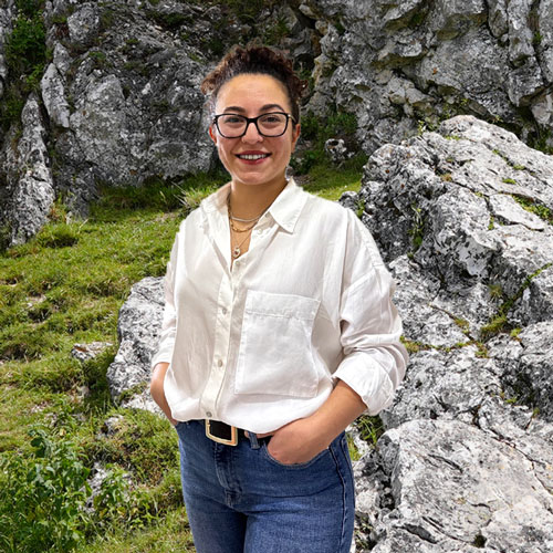 Close-up of İlayda Doğan, outdoors, in a white shirt, smiling.