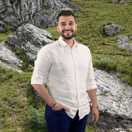 Close-up of Kadir Sert, outdoors, in a white shirt, smiling.