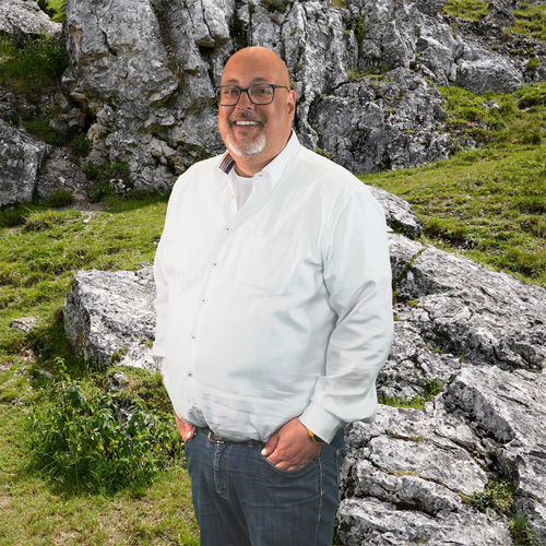 Close-up of Frank Behne, outdoors, in a white shirt, smiling.