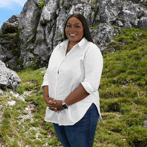 Close-up of Liniah Mumbengegwi, outdoors, in a white shirt, smiling.