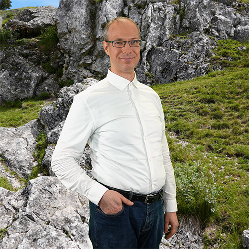 Close-up of Dr. Matthias Koitka, outdoors, in a white shirt, smiling.